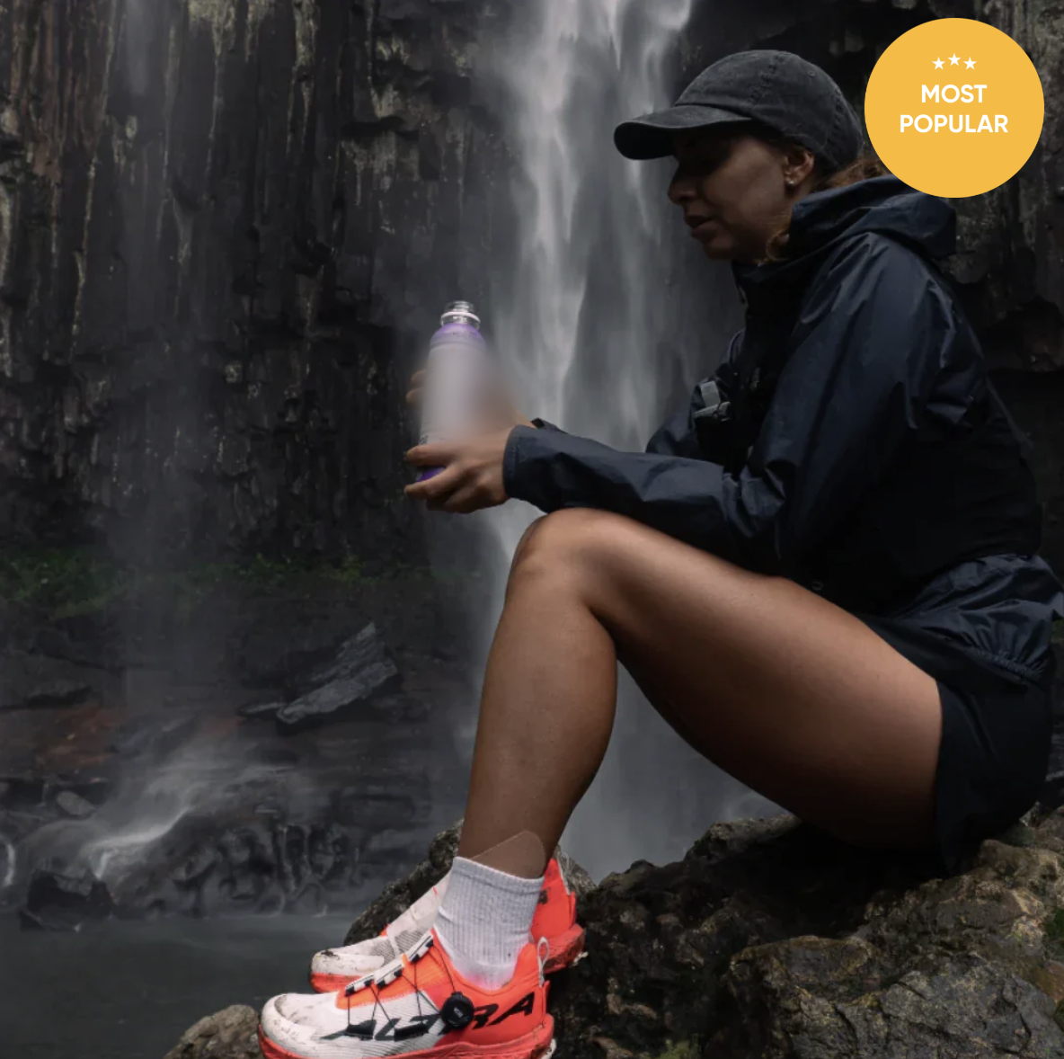 Marketing photo for a best-selling electrolyte drink: athlete resting by a waterfall holding the bottle, 'Most Popular' badge